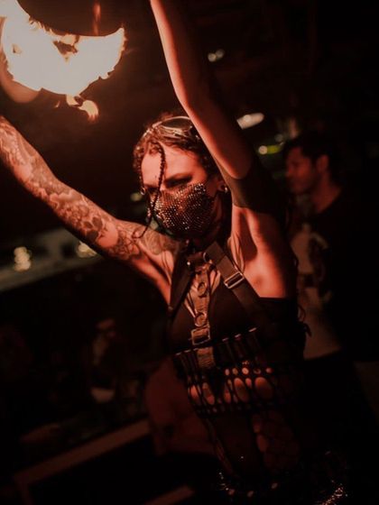 A close-up of a performer in a dark, mysterious costume with a chainmail mask, holding a fire torch. This showcases our edgier, more intense thematic looks.