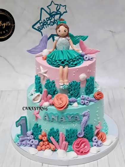 A magical mermaid-themed cake for a first birthday. This 3kg pineapple cake features a doll with a mermaid tail, sitting amidst an underwater scene of coral and seashells.