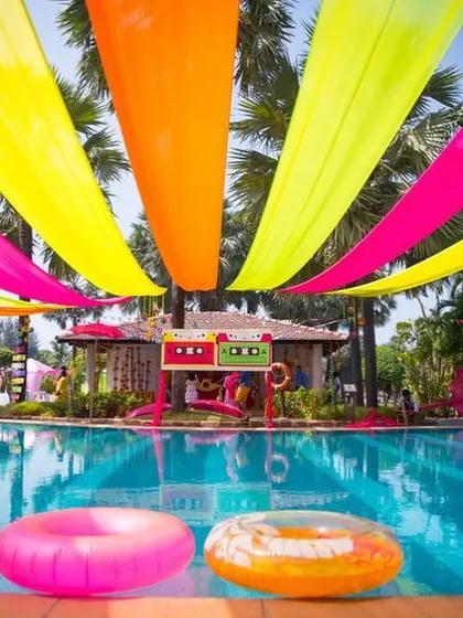 A vibrant poolside Mehndi or pool party setup with colorful drapes in neon pink, orange, and yellow. It’s all about creating a fun, carnival-like atmosphere.