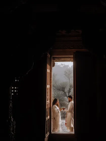 A beautifully framed shot of the couple standing in the doorway of an old heritage building. The dark foreground creates a sense of intimacy and timelessness.