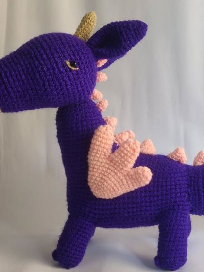 A side profile of the custom purple dragon, showing off his wings and spiky tail. Every detail is carefully crocheted to bring the client's vision to life.