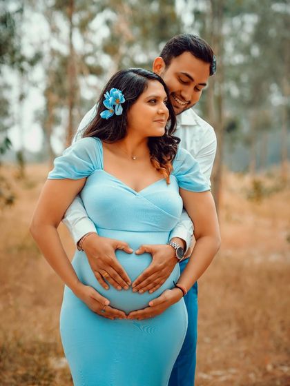 A close-up of the couple making a heart shape with their hands on the baby bump. A classic and heartfelt pose for an outdoor maternity shoot.