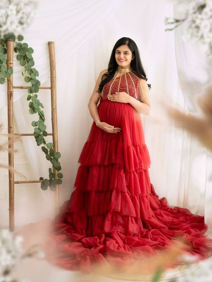 A beautiful solo portrait of a mom-to-be in a tiered red gown, set against a bright and airy studio backdrop.