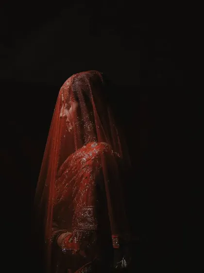 A minimalist and artistic bridal portrait. The bride is veiled and set against a pure black background, creating a sense of mystery and elegance with just her silhouette.
