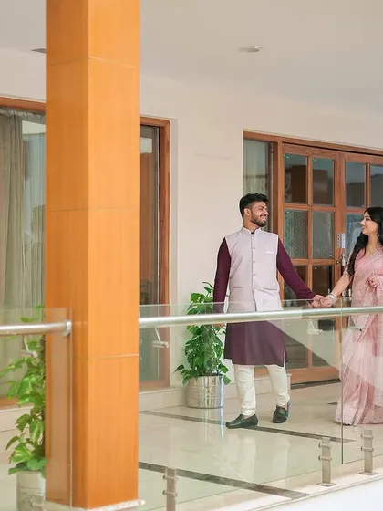 A classic shot of the couple holding hands and walking along a modern, glass-paneled balcony.
