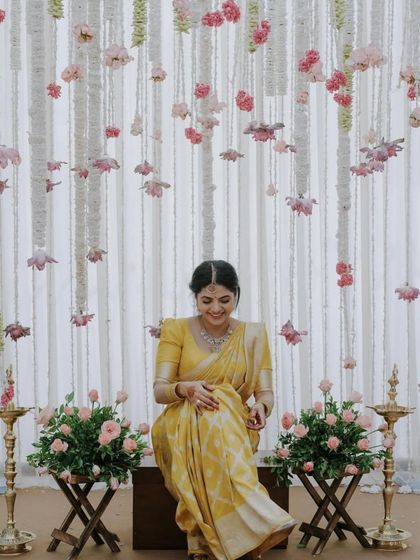 A serene shot of a client in a simple yellow saree with a matching blouse, seated amidst beautiful floral decor.