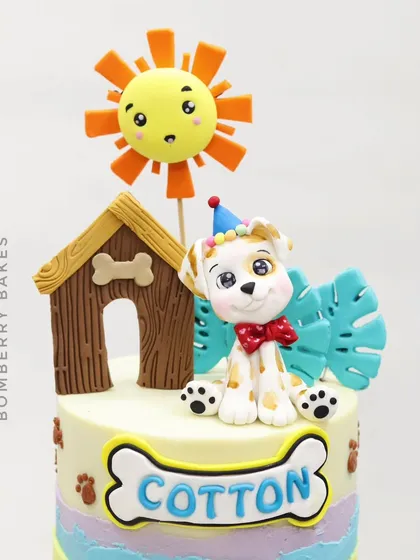 The top tier of the gravity cake, featuring a cute, edible dog figurine, a doghouse, and a smiling sun.