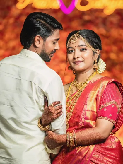 A beautiful portrait of the couple. The bride's makeup is radiant, and her red saree stands out beautifully against the warm, festive background.