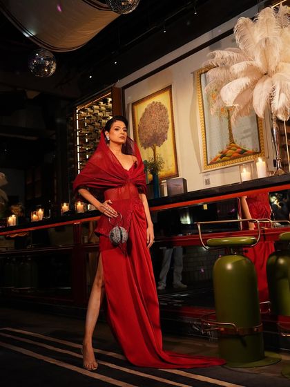 This crimson gown, with its high slit and structured hood, is captured in a moment of poised confidence, perfect for making an unforgettable entrance.