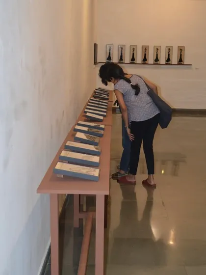 A visitor looking closely at the details in a series of reverse paintings by Shakuntala Kulkarni.