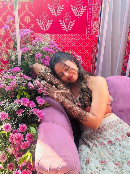 A serene bride resting amidst a sea of flowers, her beautiful mehndi on display.