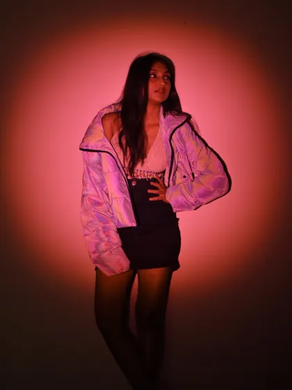 Looking away from the camera, caught in the pink spotlight. This pose has a sense of mystery and artistic flair.