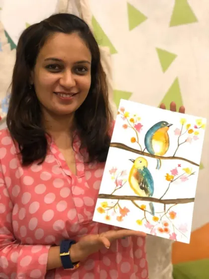 A student beaming with pride as she holds up her delicate watercolor painting of two birds. Learning to use watercolors is a gentle and rewarding process, and her joy is the perfect result.