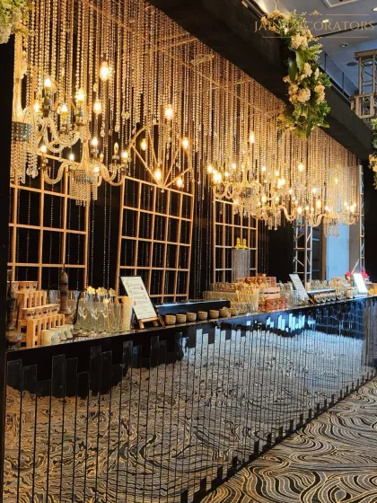 A glamorous bar setup for a grand reception. The mirrored bar front reflects the stunning ceiling of hanging chandeliers and crystals, creating a dazzling effect for guests as they order their drinks.