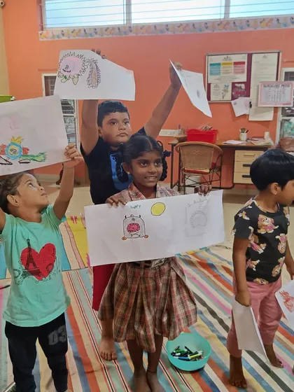 The children hold their monster drawings high for everyone to see. We celebrate every child's unique artistic expression.