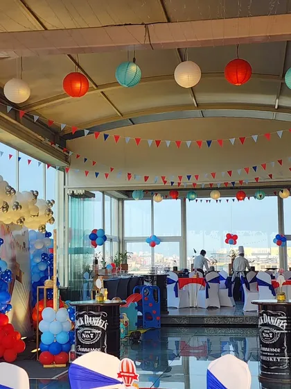 An overview of the party venue, showing the red, white, and blue color scheme carried through with hanging paper lanterns, pennant banners, and balloon arrangements, all complementing the main stage.