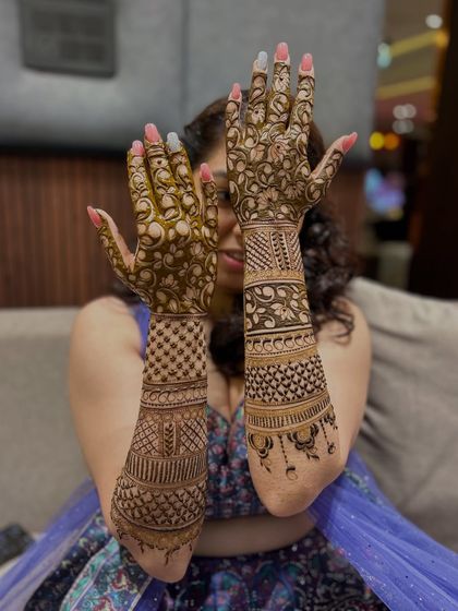 A happy bride hiding behind her beautifully adorned hands, which are covered in delicate floral and vine patterns.