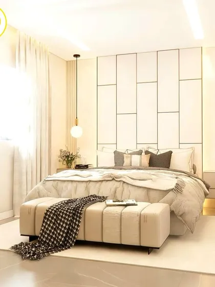 A bright and airy bedroom with a white paneled feature wall and gold accents. The design is minimalist yet luxurious, with globe pendant lights and a comfortable upholstered bench.