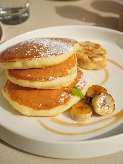 A stack of our light and fluffy pancakes, dusted with powdered sugar and served with caramelized bananas and a drizzle of syrup. A sweet treat for any time of day.