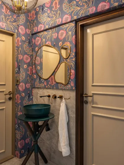 I love using powder rooms to make a bold statement. The vibrant, maximalist wallpaper paired with a unique teal basin and organic-shaped mirrors turns this small space into an unexpected jewel box of design.