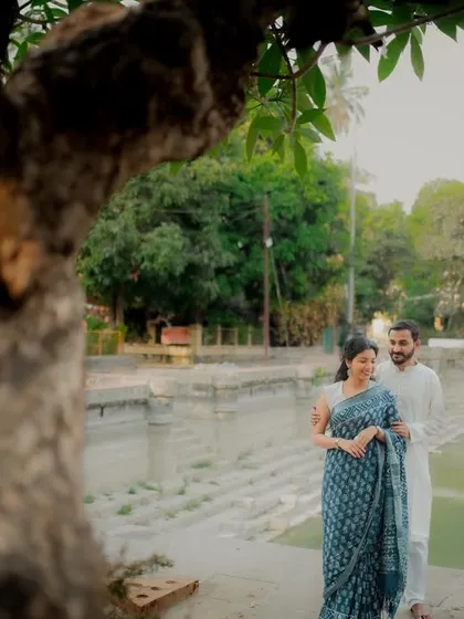 An artfully framed shot of the couple standing by a temple pond, viewed through the leaves of a tree. This composition adds a sense of intimacy and discovery to the scene.