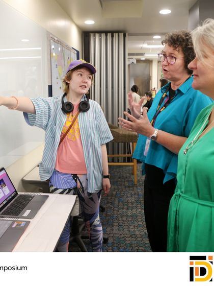 An IDI student points to details on her project board during the symposium. This event allows students to practice articulating their process and defending their work, much like in a university seminar.