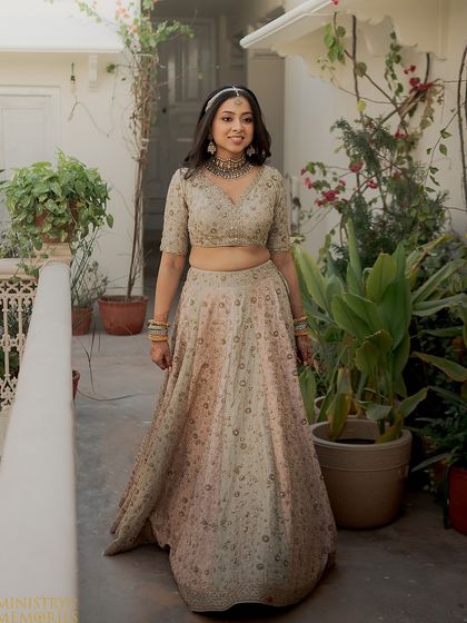 A full-length shot of the bride in her family home. The pastel lehenga and soft makeup create a look of quiet elegance.