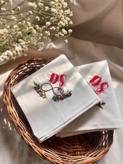 A closer look at the custom handkerchiefs, showcasing the vibrant red initials and the delicate greenery.