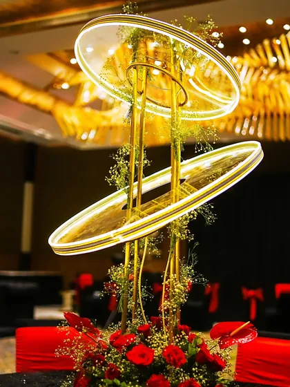 A modern, illuminated centerpiece with floating rings, set amidst a base of red roses, designed to be a conversation starter at every table.
