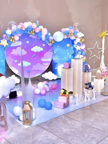 A magical 'Star & Moon' themed welcome home party. This whimsical setup includes a night-sky backdrop with custom balloon arches, illuminated stars, a crescent moon prop, and themed pedestals for the cake and gifts.