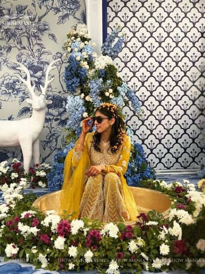 A chic and modern haldi seating area for the bride. The blue and white floral backdrop with a pop of yellow from the bride's outfit creates a picture-perfect moment that's both stylish and fun.