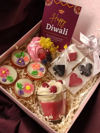A closer look at a pre-curated Diwali hamper. This box includes a Berry Cupcake Soap, Poker Party Soaps, a Berry Mousse Candle, and four Floral Tealight Candles, plus a personalized card.