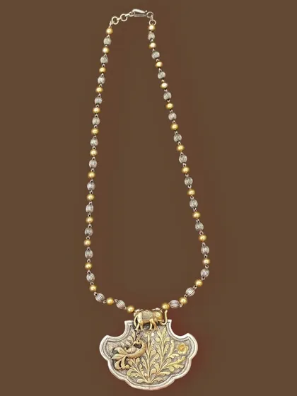 An example of my unique dual-tone work. This necklace features a silver pendant with a gold-plated floral design and an elephant motif, strung on a chain of alternating silver and gold beads.