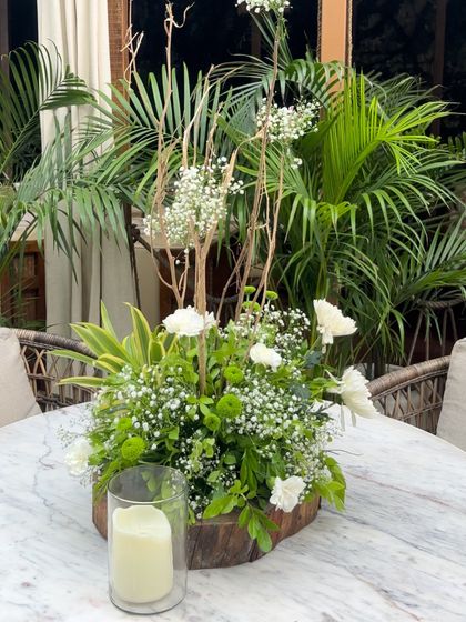 A rustic yet elegant table centerpiece for the baby shower. This arrangement on a wooden base combines fresh white flowers and baby's breath with natural branches for a touch of the outdoors.