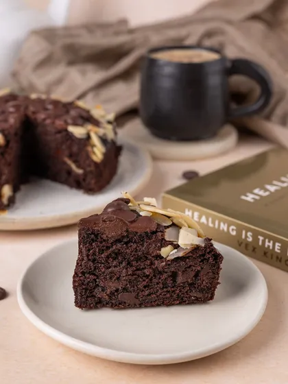 A cozy, rainy-day scene featuring a slice of chocolate cake, a hot cup of coffee, and a good book. This lifestyle approach helps customers imagine themselves enjoying the dessert.