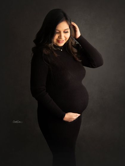 A classic and elegant portrait in a simple black dress. The soft lighting beautifully highlights the contours of her baby bump.
