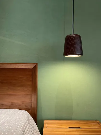 A detail of a wooden pendant lamp against a green lime-washed wall in the Worli Duplex. The choice of color and material creates a serene and natural atmosphere in the bedroom.