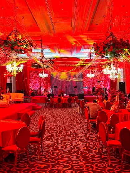 A wide shot of the reception hall, completely transformed by red lighting and decor. The tables are set with red linens and chairs, and the ceiling features hanging floral installations, creating a cohesive and intensely glamorous atmosphere.