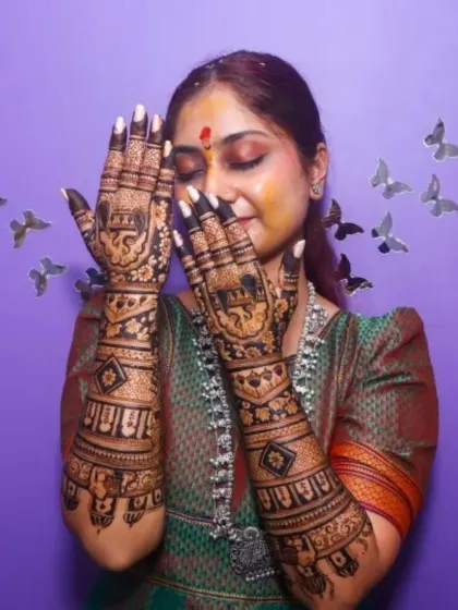 A happy bride with her full bridal mehendi, featuring traditional elephant motifs on the palms and extending up the arms.