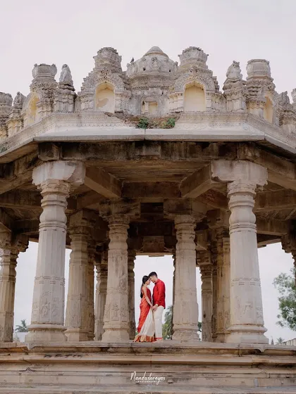 Framed by the magnificent stone pillars of a heritage temple in Melukote, a couple shares an intimate moment, their vibrant red outfits a beautiful contrast to the ancient stone. This shot showcases my love for blending romance with history.