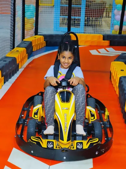 This young driver is focused and ready to go, sitting in her yellow go-kart on our vibrant orange track.