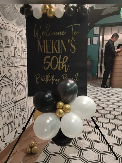 A personalized welcome easel for a 50th birthday bash. The black and gold design sets a sophisticated tone for the event, complemented by a simple yet elegant balloon cluster that matches the party's color scheme.
