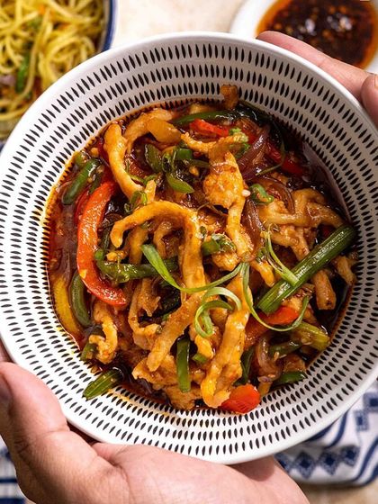 A comforting bowl of my shredded chicken stir-fry held in two hands. This dish is packed with colorful vegetables and coated in a delicious sauce, perfect with a side of noodles.