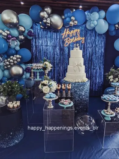 For a truly glamorous and striking celebration, I designed this deep blue and silver themed dessert station. The setup includes a metallic blue fringe curtain, a full balloon arch, and clear acrylic stands to display the cake and treats, making everything look like it's floating.