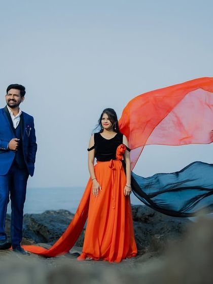 The wind catches the two-toned trail of this gown, creating a dramatic and artistic pre-wedding photo on the rocky shore.