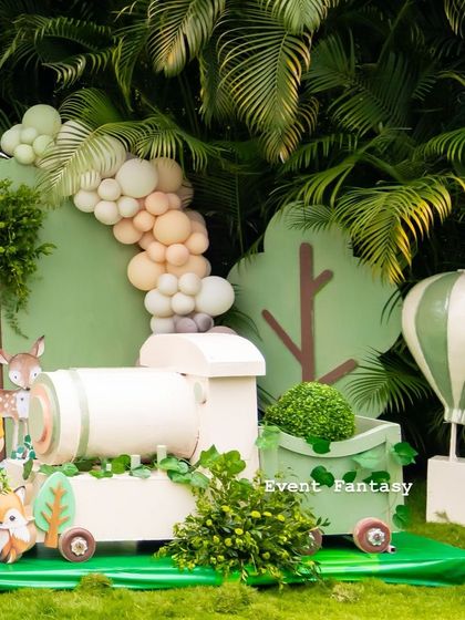 A wooden train and hot air balloon prop set against a backdrop of lush palm trees, blending the woodland theme with the natural surroundings.