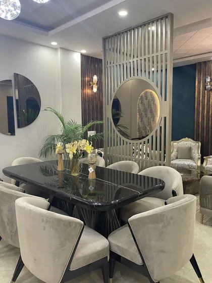 An elegant dining setup featuring a black marble-top table, plush velvet chairs, and a statement partition with a circular mirror. This design is perfect for creating a sophisticated space for family meals and entertaining.