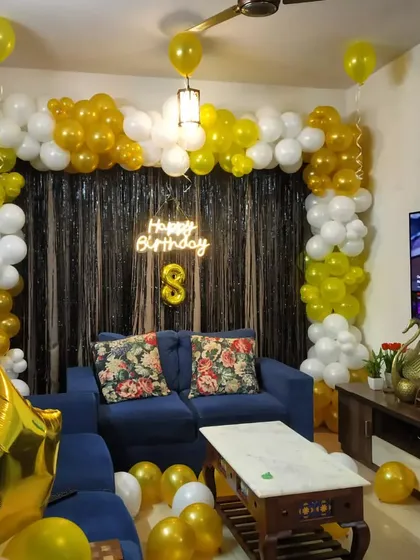 A yellow and white balloon arch with a neon sign for an 8th birthday, elegantly arranged around a living room sofa.