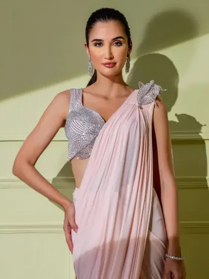 A soft and romantic look. This baby pink drape saree is paired with a silver sequined blouse, featuring a 3D floral detail on the shoulder.