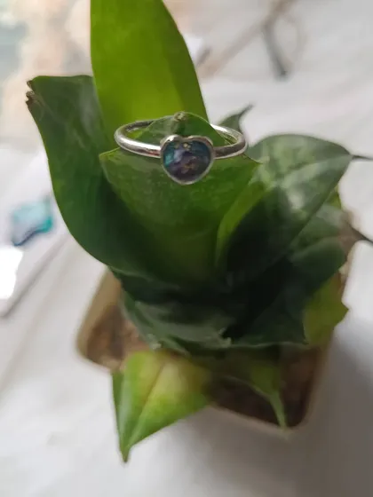 A delicate heart-shaped ring made from preserved orchid petals, resting on a green leaf. It shows how even a small piece of jewelry can hold a big memory.